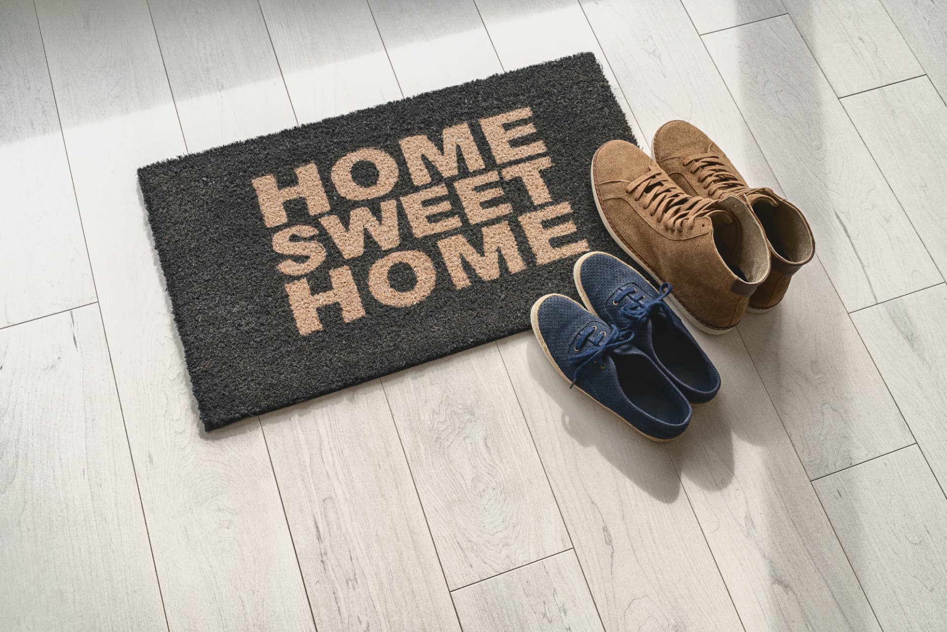 A 'Home Sweet Home' doormat with two pairs of shoes beside it