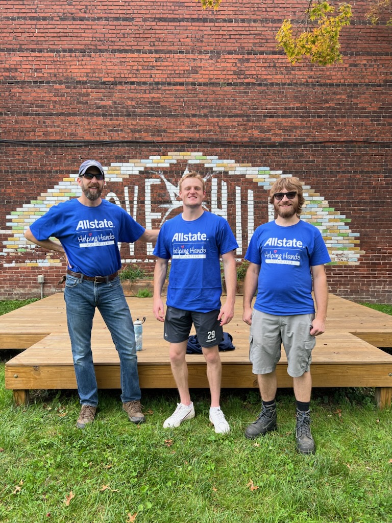 Three volunteers standing in front of a brick mural next to a newly built wooden deck