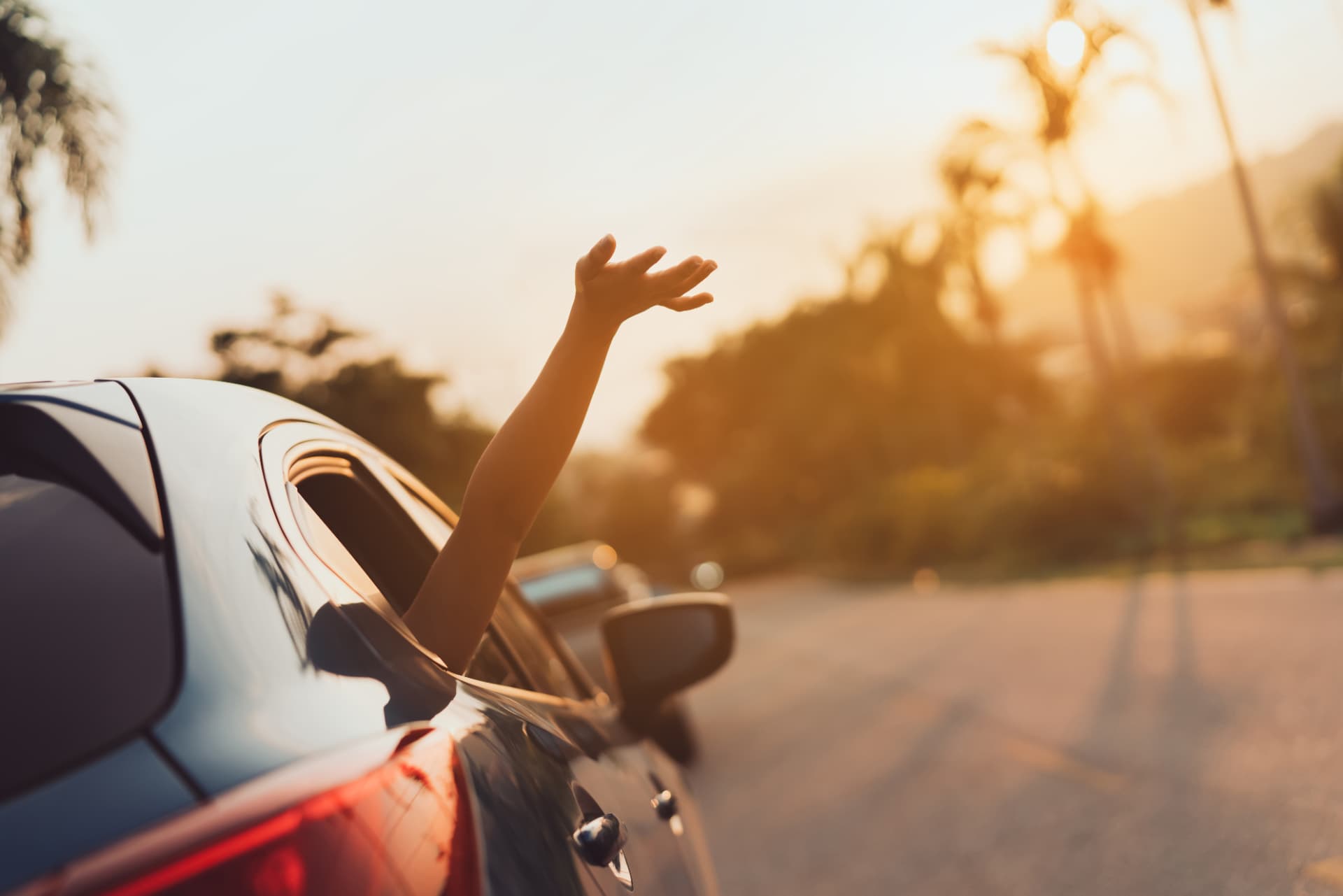 A hand reaching out of a car window into the sunset