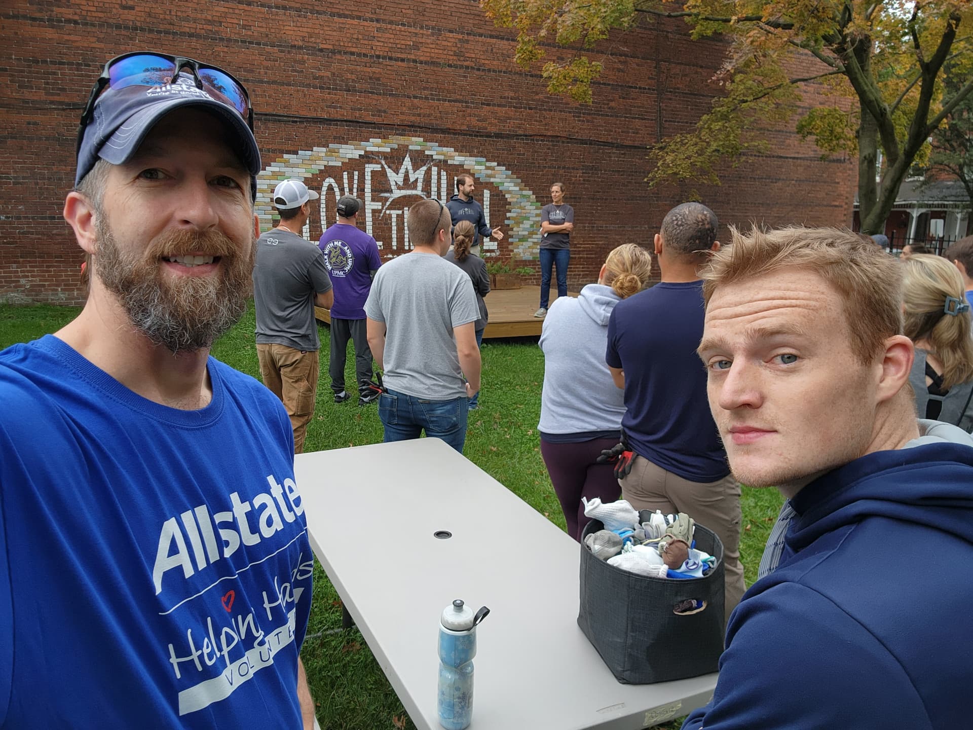 Volunteers gathered in a park in front of a painted brick mural before a service project