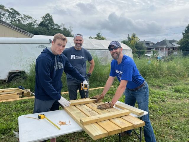 Volunteers assembling a wooden picnic table beside a greenhouse